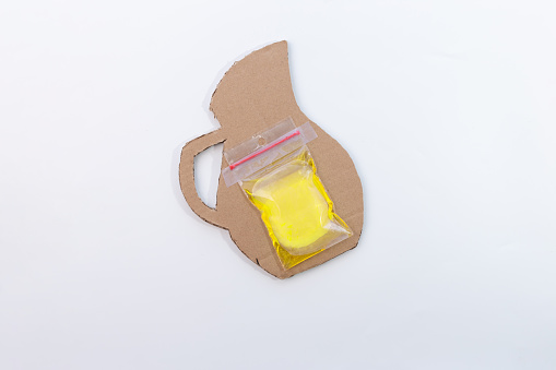 a freezer bag containing yellow liquid is taped to a cardboard piece of lemonade pitcher craft, part of making process, DIY, tutorial, project for kids, easy summer craft from recycled paper,
