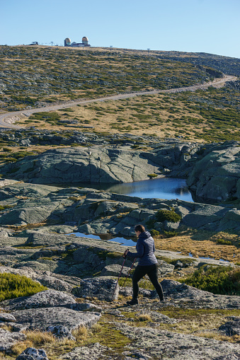 Hiking person in rocky landscape of high plateau of Torre with dome buildings in background on a sunny autumn day, Torre, Serra da Estrela, Portugal