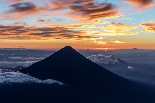 Silhouette of volcano de agua at firey orange sunrise or sunset seen from the top of volcano de acatenango, guatemala