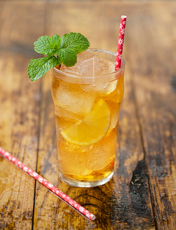 glass of ice tea with mint and lemon on wooden table