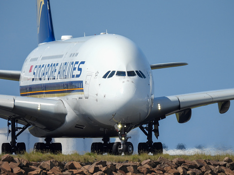 A Singapore Airlines Airbus A380-841 plane, registration 9V-SKN, taxiing after landing at Sydney Kingsford-Smith Airport as flight SQ231 from Singapore.   In the background are fuel storage tanks.  This image was taken from near Kyeemagh Beach, Botany Bay on a hot and sunny morning on 24 March 2024.