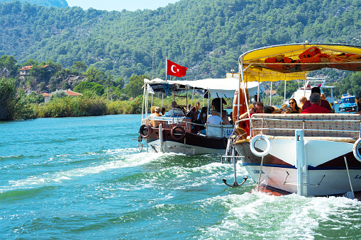 Tourist pleasure boats with Turkish flag on Dalyan River, next to rocks, which contain the Lycian tombs, in Mugla Province on south-west coast of Turkey.