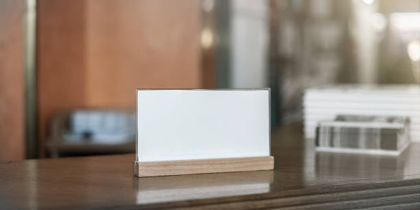 Small white blank card displayed on wooden holder on dark countertop with blurred interior background. Perfect for point of sale promotions, price tags, or table reservations in a cozy setting.