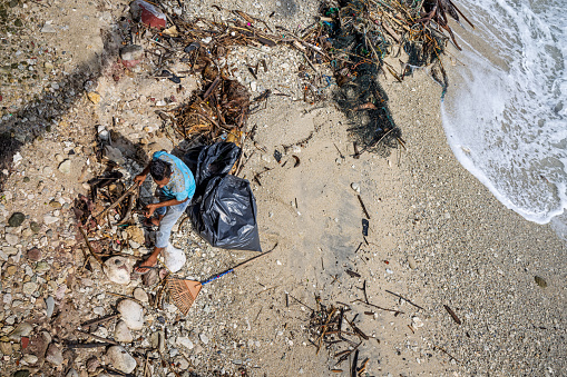 Sabang, Pulau Weh, Indonesia - January 11th 2024: Man collecting garbage on the beach at the Malacca Strait on the island Weh north of Sumatra