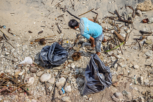 Sabang, Pulau Weh, Indonesia - January 11th 2024: Man collecting garbage on the beach at the Malacca Strait on the island Weh north of Sumatra