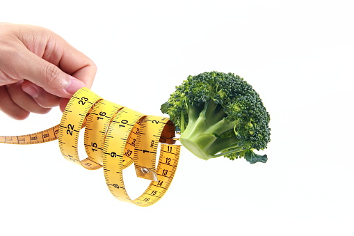 Man hand holding a fork with broccoli and tape measure