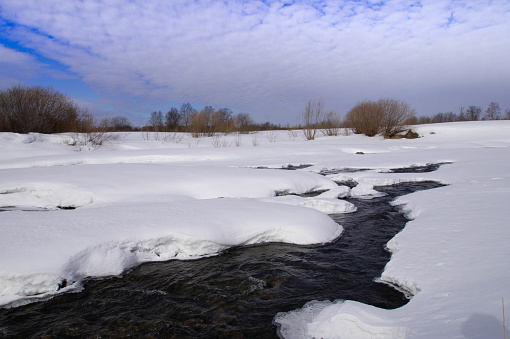 A thawed river and cumulus clouds in the sky. Spring landscape.
