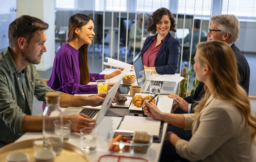 Multiracial group of people, coworkers working on laptop, chatting and making plans during lunch time in office kitchen. Business and career concept.