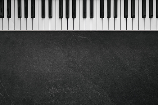 Musical keyboard, piano keyboard on a textured black background. Flat lay, space for text. Minimalistic music background, conceptual minimalism.