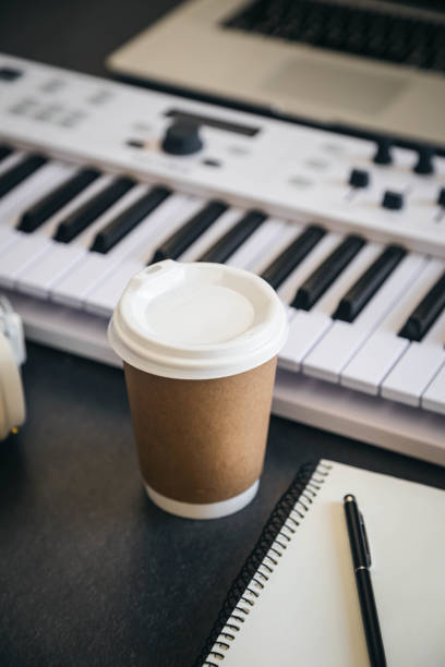 istock Musician workplace table with paper cup and white piano keyboard. 2109023310