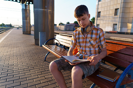 a student poses at a railway station, a boy is waiting for a train on the platform, reading books and doing homework, goes to study, the concept of education