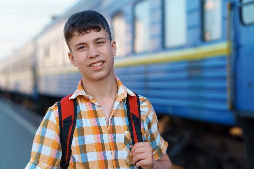 a student poses at a railway station, a teenage boy walks along the platform to the train, he has a backpack and books, goes to study, the concept of education