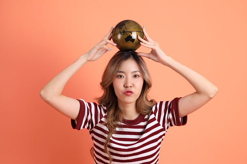 The young Asian woman in casual clothes with gesture of holding a globe on the orange background