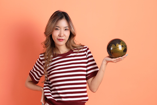 The young Asian woman in casual clothes with gesture of holding a globe on the orange background