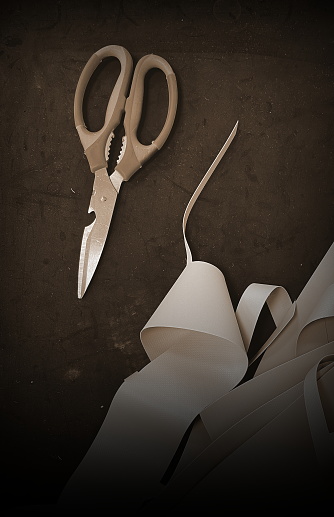 Sepia-Toned Scissors And Curled Paper Strips On Dark Textured Background