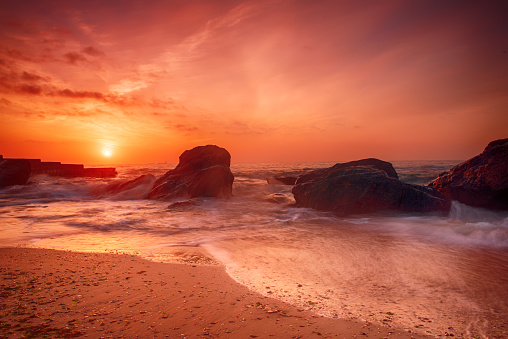 Summer seasonal natural vacation background. Romantic morning at sea. Big boulders sticking out from smooth wavy sea. Pink horizon with first hot sun rays. Long exposure.