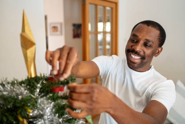 istock Happy african man decorating a Christmas tree at home 2109188903