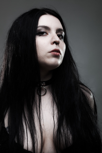 Goth girl with white eyes and long dark hair against dark gray background.