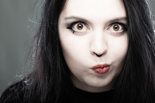 Close up portrait of a goth style girl looking at camera against gray background