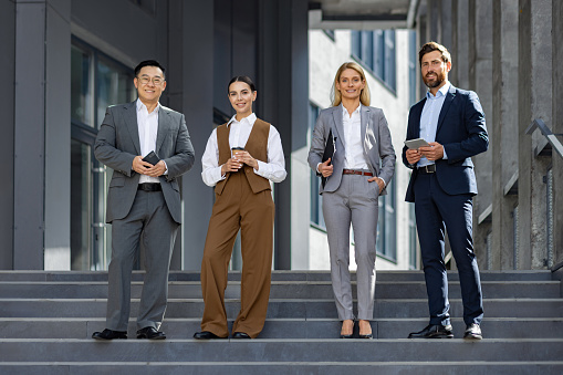 A group of smartly dressed corporate professionals are seen taking a pause from work on the steps outside their workplace, embodying teamwork, success, and city business life.