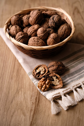 Indulge in the simple pleasure of walnuts nestled in a bowl, their rich brown shells contrasting against a soft white cloth beneath. The wooden surface provides a rustic backdrop, adding to the charm of this close-up shot. A few walnuts spill out, inviting you to savor their natural beauty up close. Immerse yourself in the essence of wholesome goodness captured within this delightful composition.