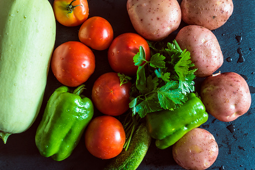 Heap of fresh vegetables (tomatoes, bell pepper, cabage, cucumber, parsley, potatoes) on a black background;