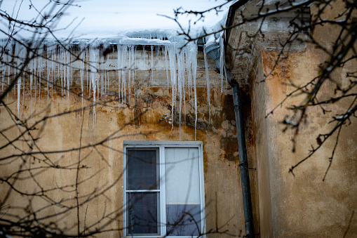 Big beautiful icicles hang from the snow-covered roof in front of the windows of the house. Snow on the roof