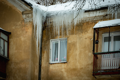 Big beautiful icicles hang from the snow-covered roof in front of the windows of the house. Snow on the roof
