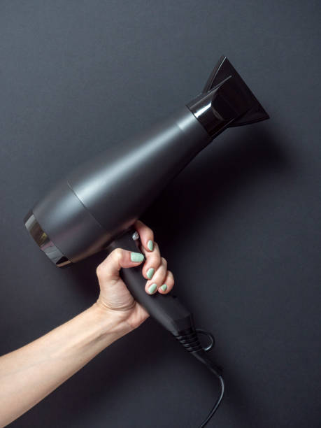 istock A woman's hand holds a black hair dryer on a black background. Accessory for beauty, Vertical photo 2109304544