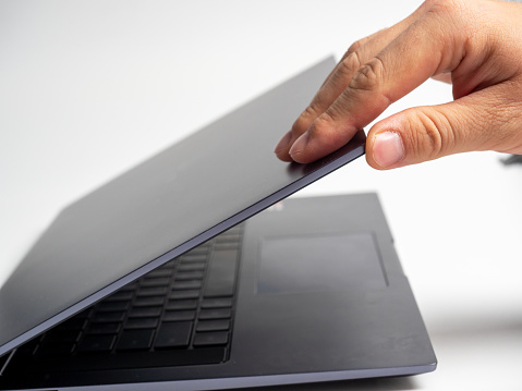 Close-up of a man's hand opening the lid of a gray laptop. Modern devices for work and leisure