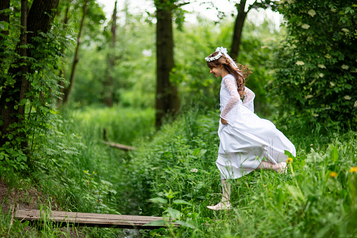 Portrait of a little girl running through a green forest. The girl is wearing a white communion dress.
Shot with Nikon D800