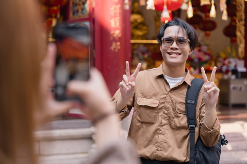 Man with a backpack smiles while being photographed against a backdrop of vibrant Chinese temple decorations.