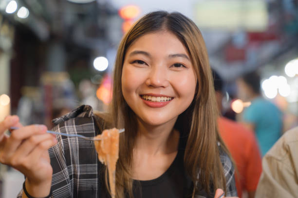 istock Happy Woman Sampling Food at Night Market. 2109325788