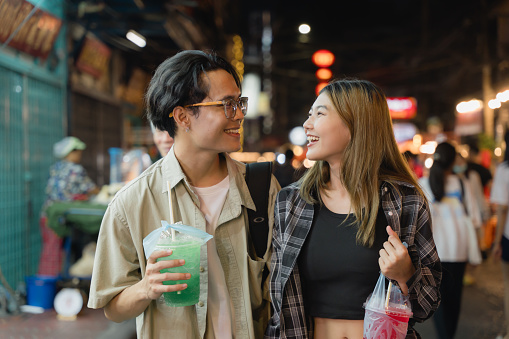 Couple enjoys refreshing beverages while strolling through the lively ambiance of a night market.