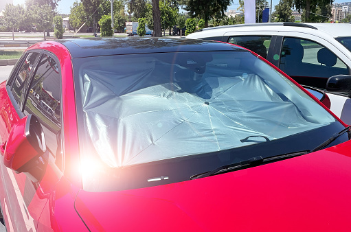 Protective reflective surface under the windshield of the passenger red car parked on a hot day, heated by the sun's rays inside the car