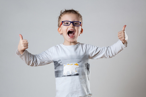 A young boy, wearing glasses, enthusiastically gives a thumbs up gesture