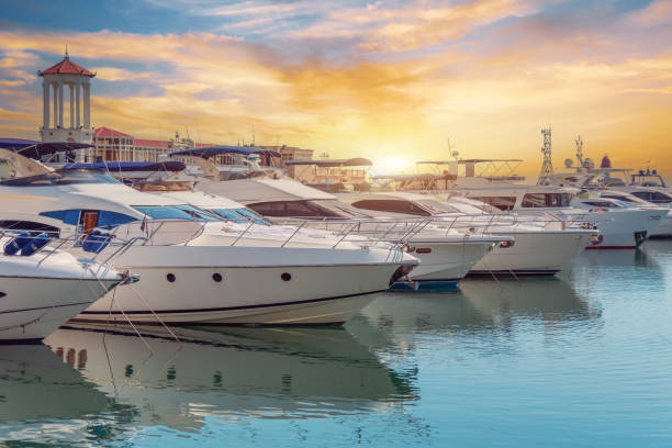 The blue water reflects orange sunset sky. Rows of sailing yachts, motor boats and fishing boats. The water area of port The blue water reflects orange sunset sky. Rows of sailing yachts, motor boats and fishing boats. The water area of port. Marina stock pictures, royalty-free photos & images