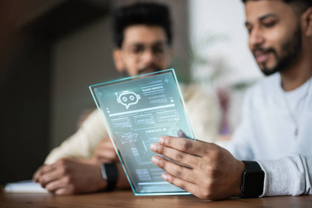 Two Indian men working together on a tablet with digital projection screen with hologram representing technologies of the future. Working on AI Chatbot development and accebility