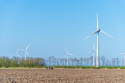 enormous wind turbines with a tractor in the foreground plowing his land
