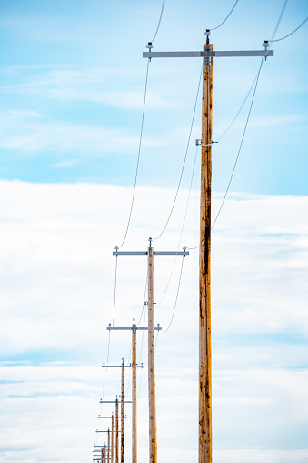 Portrait view of a row of telephone poles made of wood with cables isolated against a blue sky background in North America.