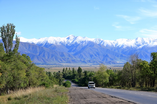 August 29 2023 - Karakol in Kyrgyzstan: street with cars to the snowy peaks behind the town