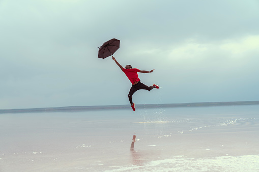 man jumping against the sun on the beach with an umbrella in his hand