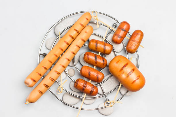 Close up, front view of a hand of a cook preparing delicious bratwurst sausages on a gas grill at a concession stand of a Christmas market.