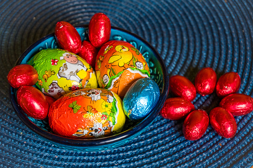 Multi-colored chocolate eggs in a blue bowl, seasoned for the feast of Easter. Easter Background. High quality photo