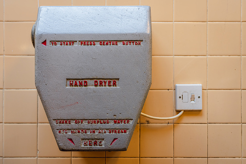 A very old hand dryer on a tiled wall