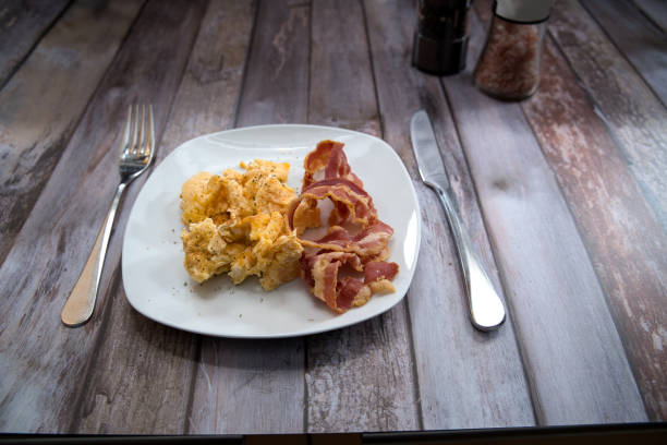 scrambled eggs with bacon on a plate. on the table are a salt mill and a pepper mill for seasoning. view from the side, point of view