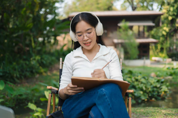 istock A woman wearing headphones is writing in a notebook 2109645698