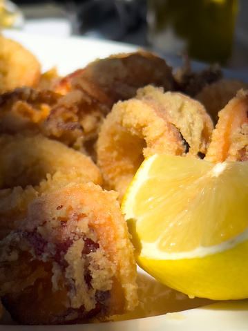 Grilled delicious Greek style calamari and lemon on plate. Sunlight falling on the food. Mediterranean diet