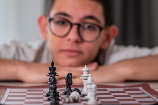 Young man in eyeglasses sitting and thinking while looking at chessboard during his game in leisure game