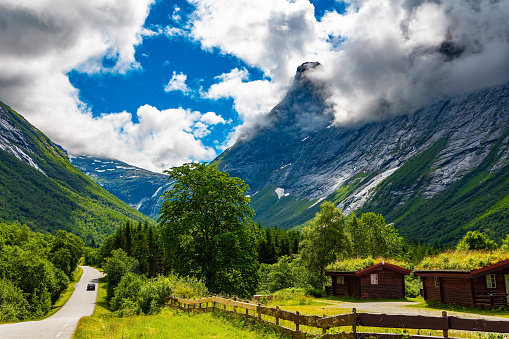 Scenic road in the mountains. Gorgeous sunny weather in Norway. Wonderful fresh green vegetation and lush snow-white clouds. Travel to fabulous Scandinavia.